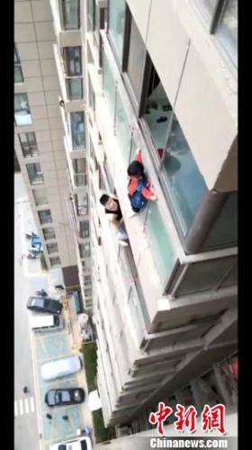 男童悬挂在半空中,非常危急,周少亭爬出窗外试图救助。视频截图